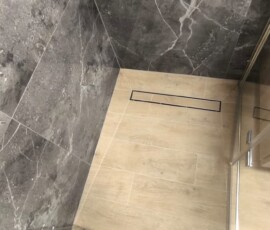Wykończenie strefy prysznicowej z płytkami imitującymi marmur i ergonomicznym układem dla osób starszych.