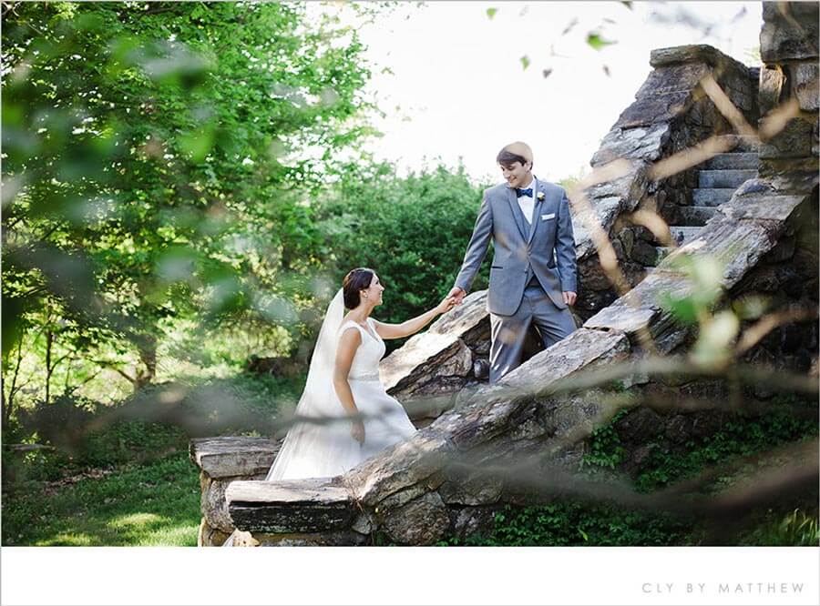 Bride and groom holding hands on rustic stone steps in a scenic garden setting.