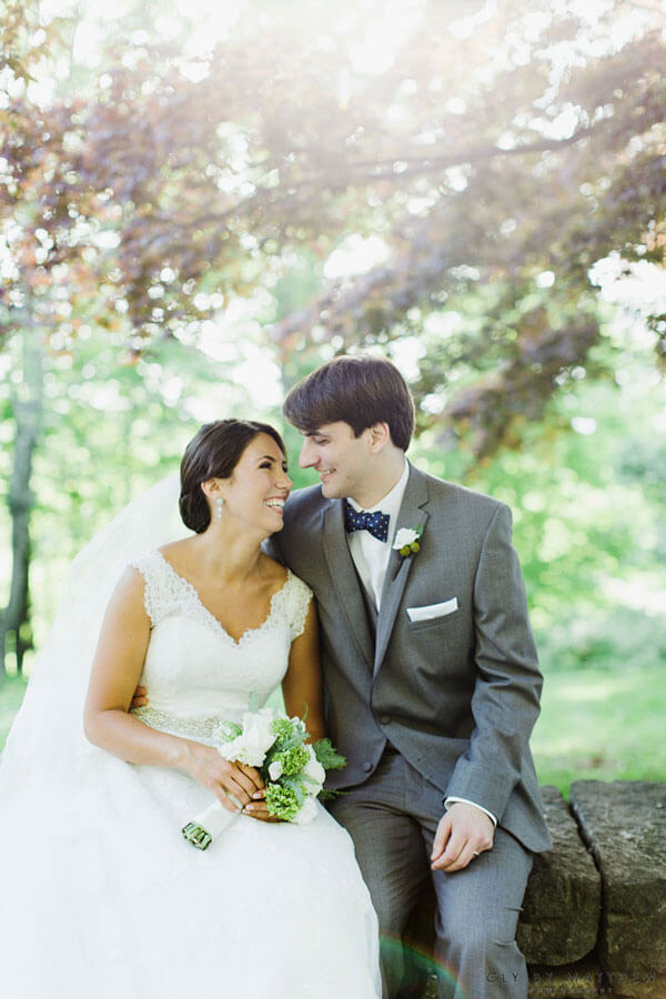 Bride and groom sharing a joyful moment beneath sunlit trees in a garden setting.