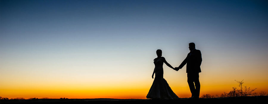 Bride and groom holding hands in a romantic sunset wedding silhouette.