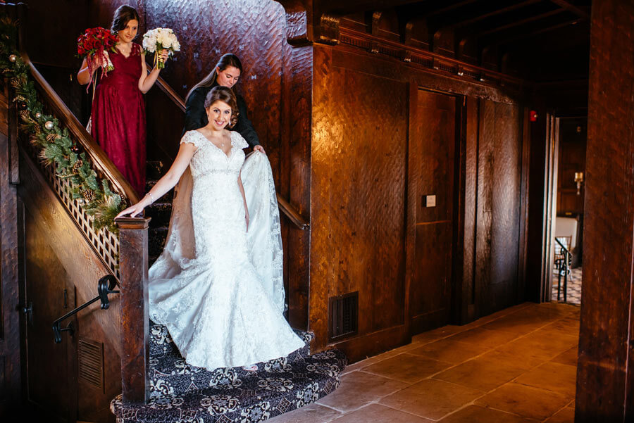 Bride descending a grand staircase with attendants in an elegant wedding venue.