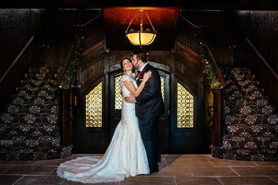 Bride and groom embracing beneath a grand staircase in an elegant wedding venue foyer.