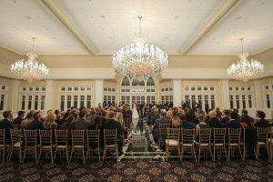 Grand indoor wedding ceremony with crystal chandeliers and guests seated along the aisle.