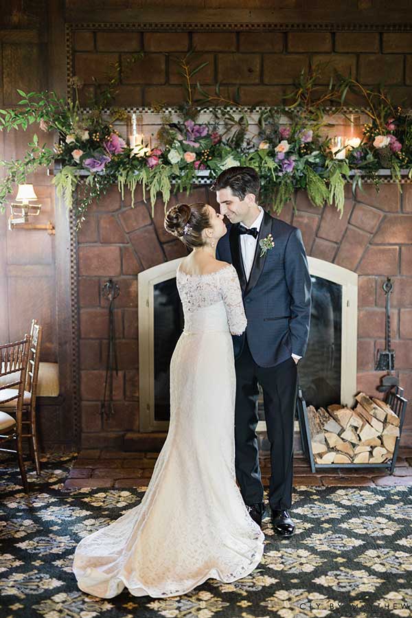 Bride and groom sharing a romantic moment by a floral fireplace at the venue.