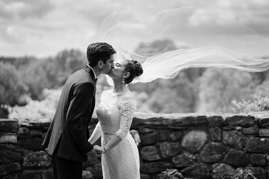 Bride and groom sharing a kiss with a flowing veil at an outdoor wedding venue.