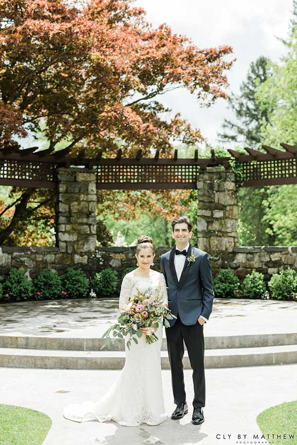 Bride and groom posing at an outdoor wedding ceremony space with a stone pergola.