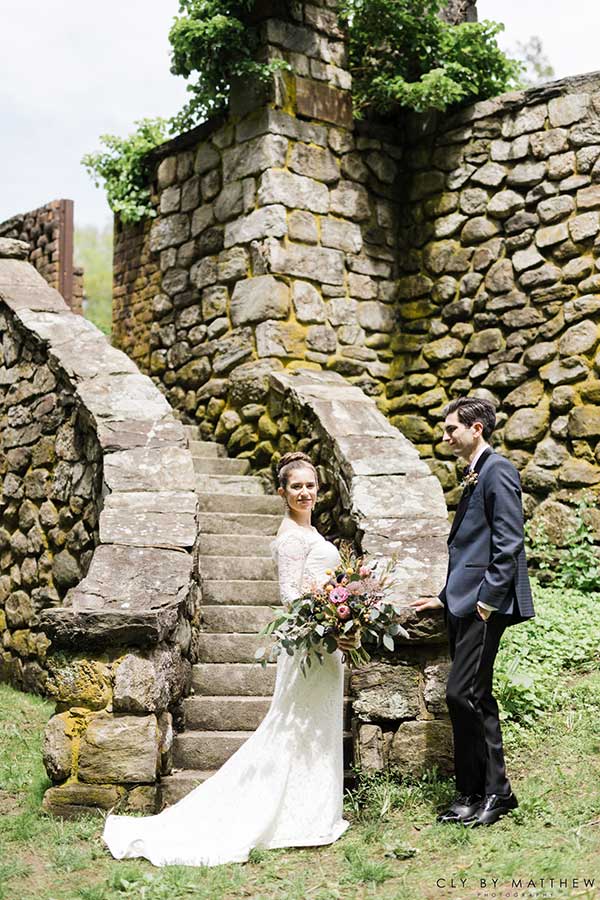 Bride and groom posing beside historic stone staircase at Le Chateau wedding venue grounds