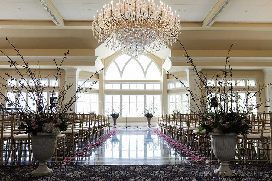 Elegant indoor wedding ceremony setup with floral aisle décor and crystal chandeliers.