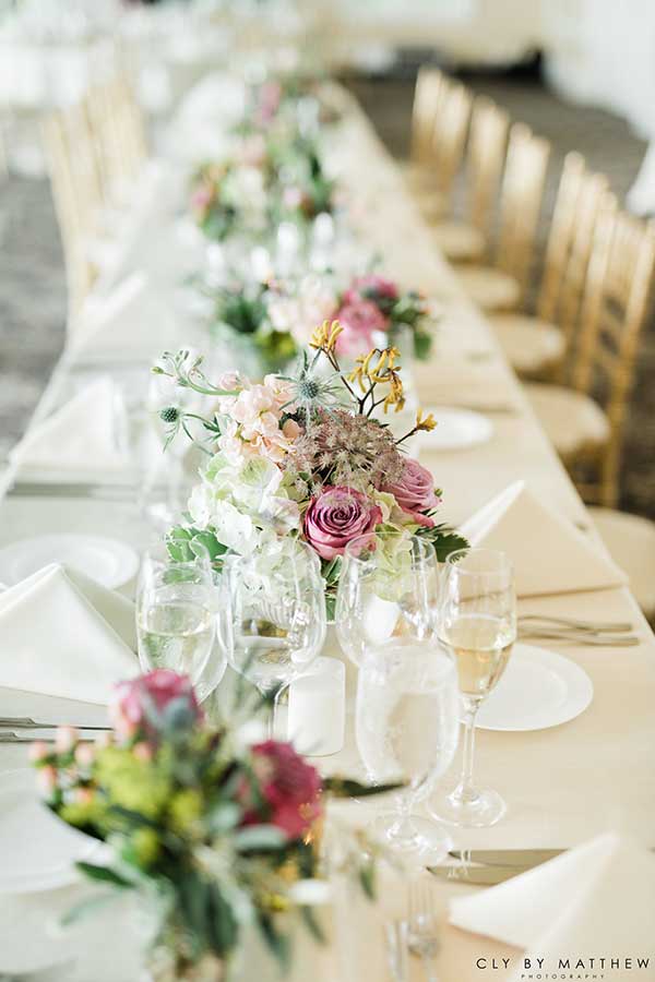 Elegant wedding reception table with floral centerpieces and formal place settings.
