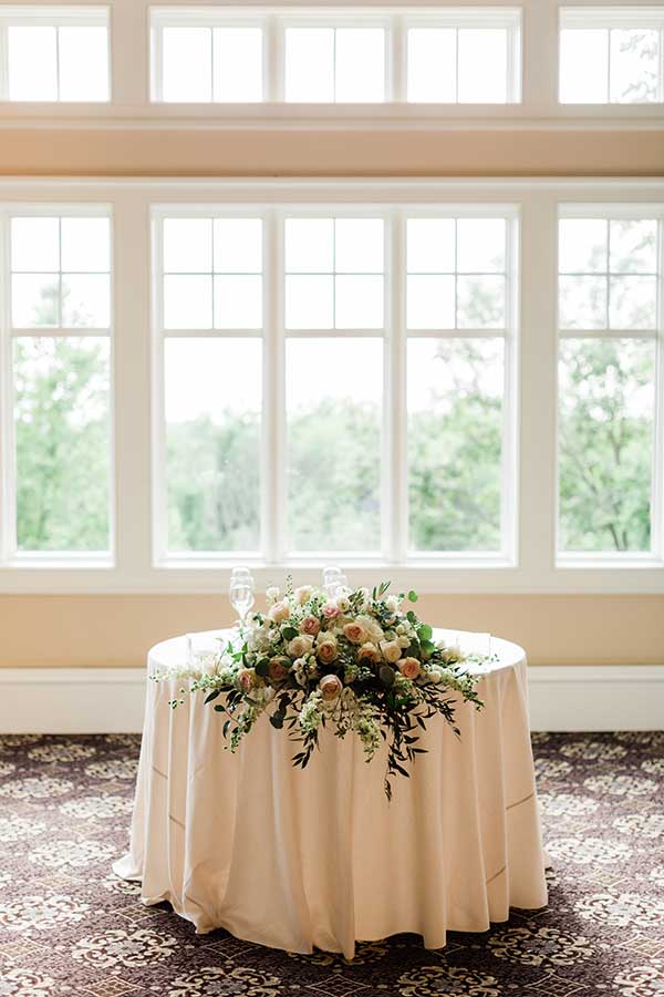 Elegant sweetheart table with floral centerpiece in a bright reception hall.