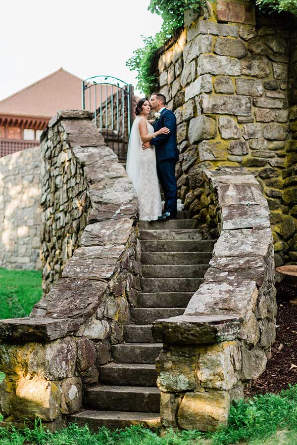 Bride and groom embracing on historic stone staircase at Le Chateau wedding venue grounds