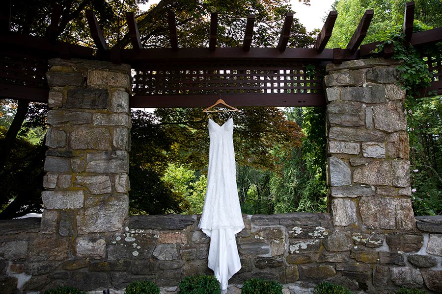 Wedding gown elegantly displayed beneath a stone pergola at Le Chateau Banquets gardens