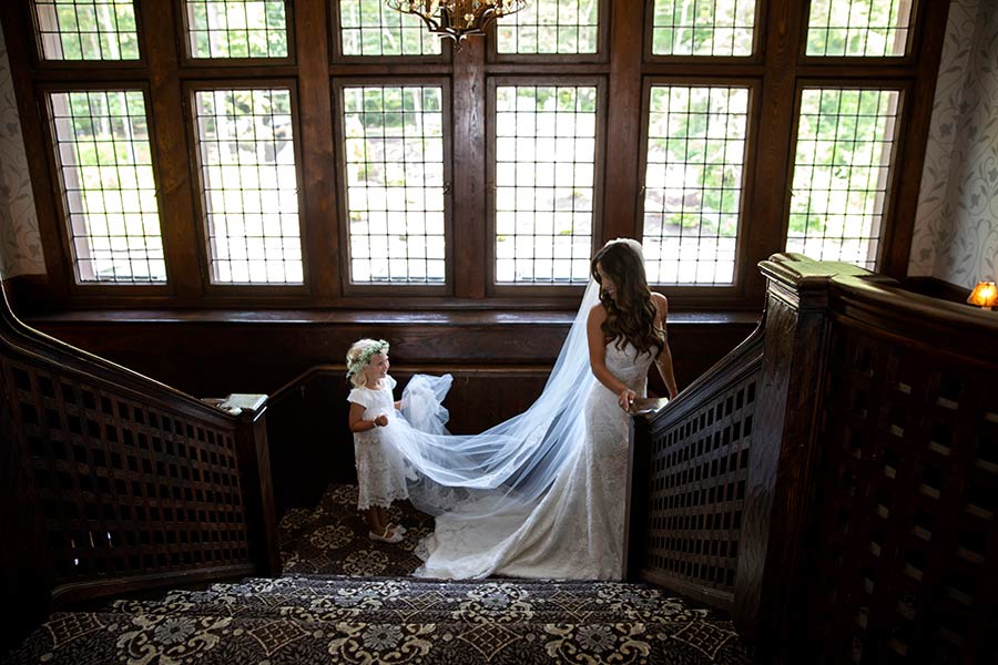 Bride and flower girl on a grand staircase with flowing veil in an elegant venue.