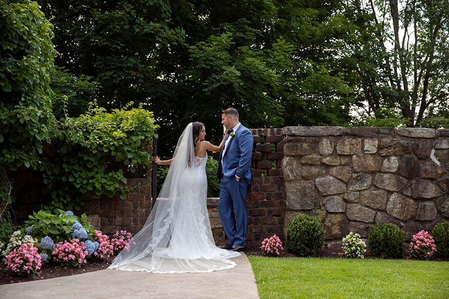 Bride and groom sharing a moment beside stone garden wall at Le Chateau wedding venue