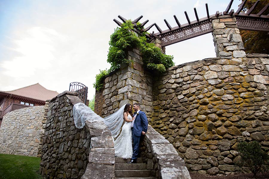 Bride and groom on historic stone staircase with flowing veil at Le Chateau wedding venue grounds
