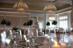 Elegant wedding cake display in a grand ballroom with crystal chandeliers and candlelight.