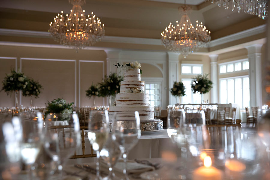 Elegant wedding cake display in a grand ballroom with crystal chandeliers and candlelight.