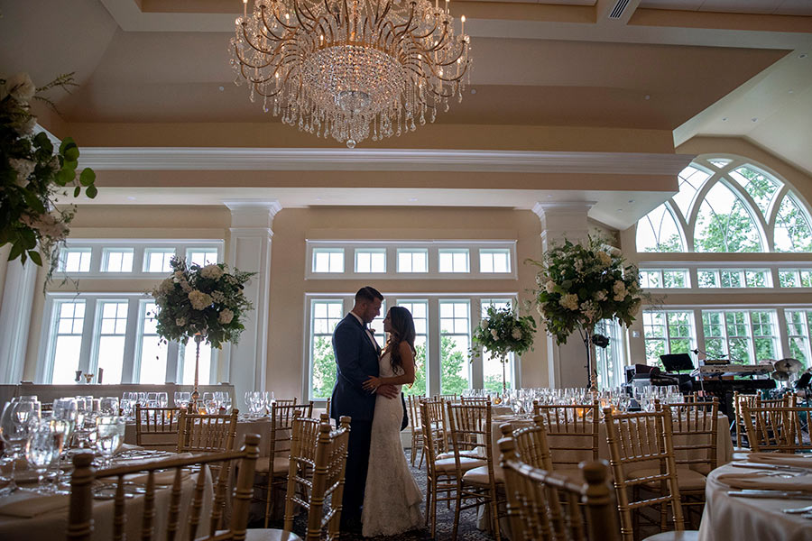Bride and groom embracing in an elegant ballroom with crystal chandeliers overhead.