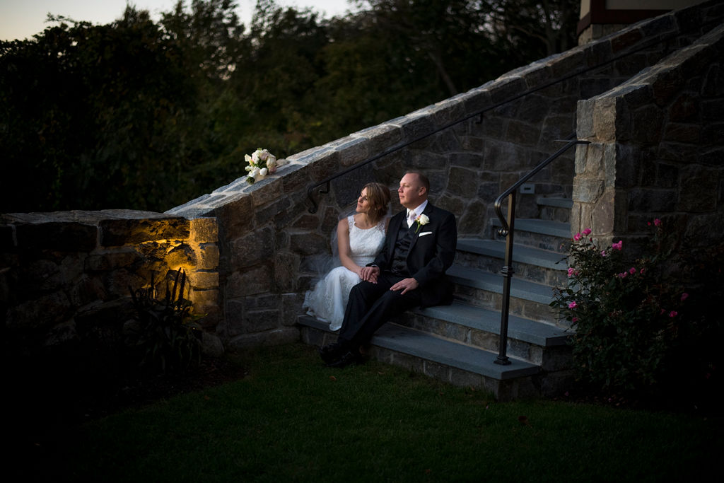 Bride and groom seated on stone steps during an elegant outdoor wedding portrait.