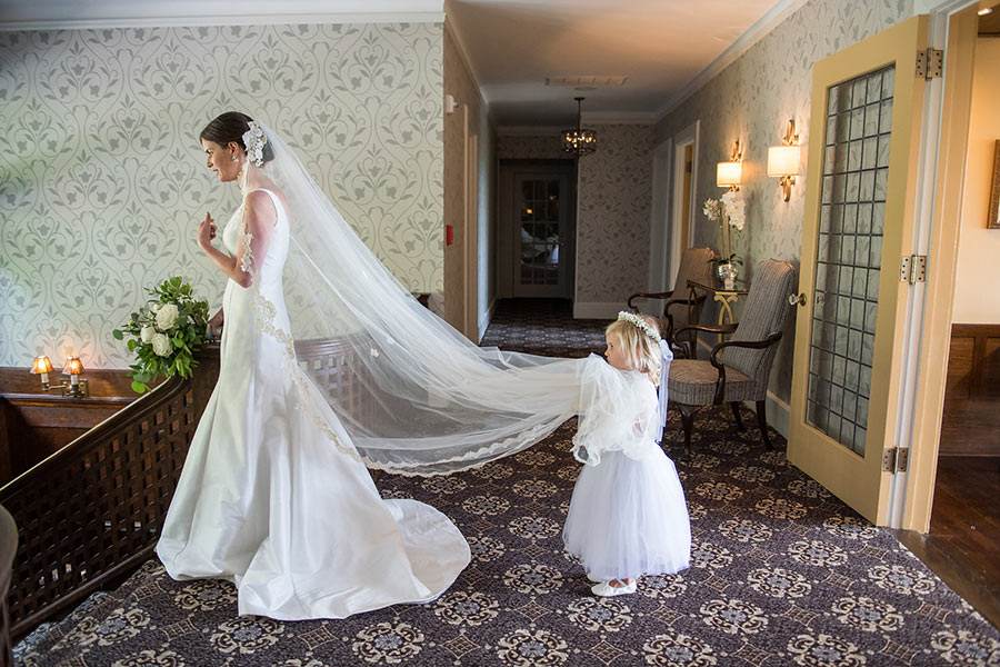 Bride with flowing veil and flower girl preparing for a wedding ceremony.