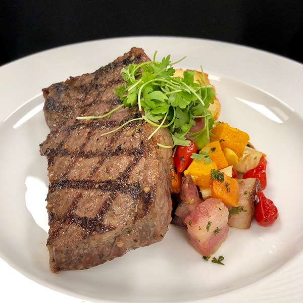 New York strip steak with roasted vegetables and herb garnish.