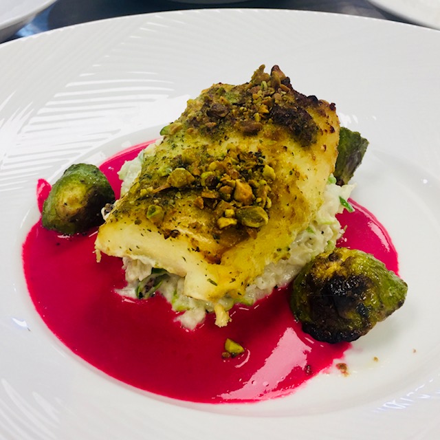 Pistachio-crusted cod served with risotto, vegetables, and vibrant beet sauce.