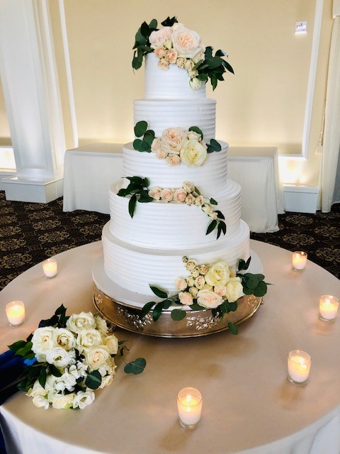 Elegant tiered wedding cake adorned with white roses and greenery accents.