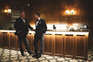 Grooms standing by elegant wood bar at Le Chateau wedding reception venue