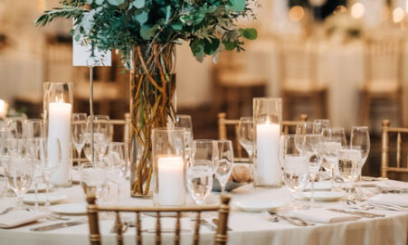 Elegant wedding table setting with tall greenery centerpiece and pillar candles.