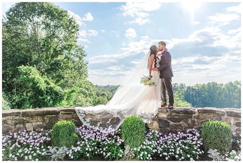 Bride and groom sharing a kiss on a stone terrace overlooking the West Garden landscape.