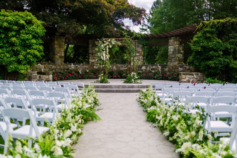 Outdoor wedding ceremony area with floral aisle and stone garden backdrop
