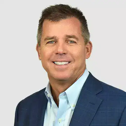 A professional headshot of a smiling man in a blue suit and light blue shirt against a plain background.