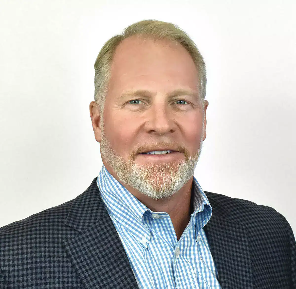 Headshot of a middle-aged man with a beard, wearing a checkered blazer and blue shirt, smiling at the camera.