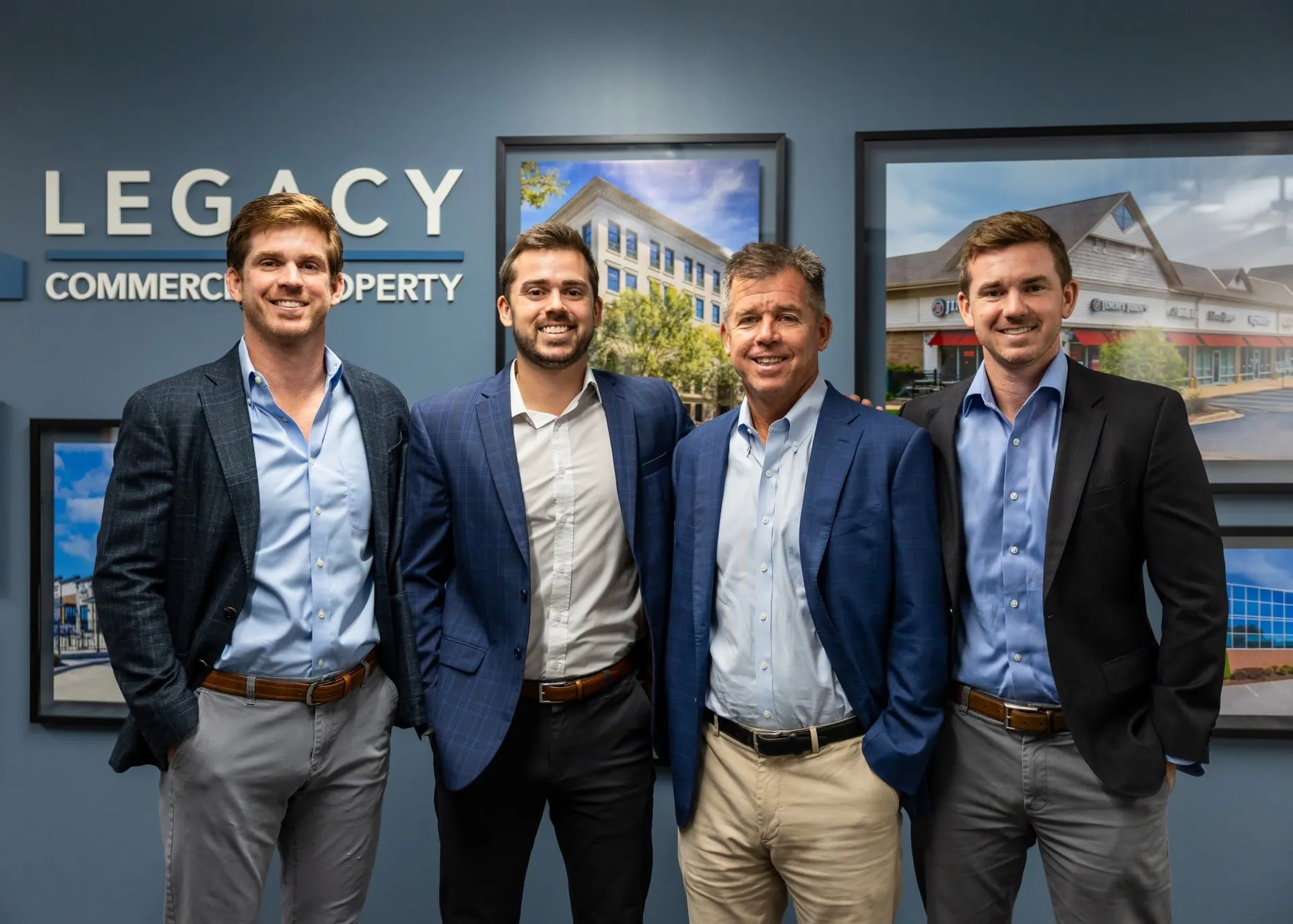 Four men in business attire standing together at a commercial property event, smiling for the camera.