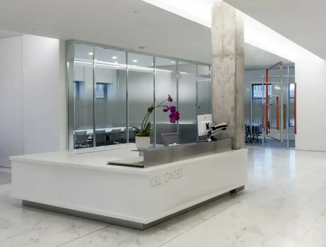 Contemporary airport check-in counter with a white surface, a computer, and a potted orchid plant, set in a sleek, minimalist environment.