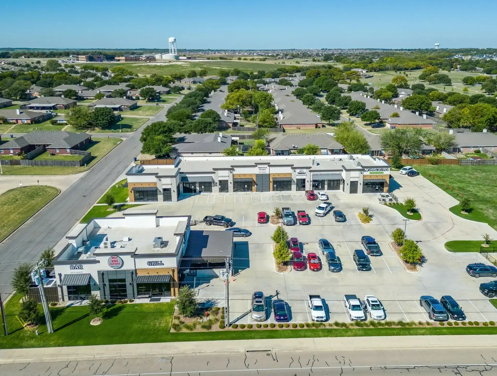 Aerial view of a commercial shopping center with parking lot and surrounding residential neighborhood.