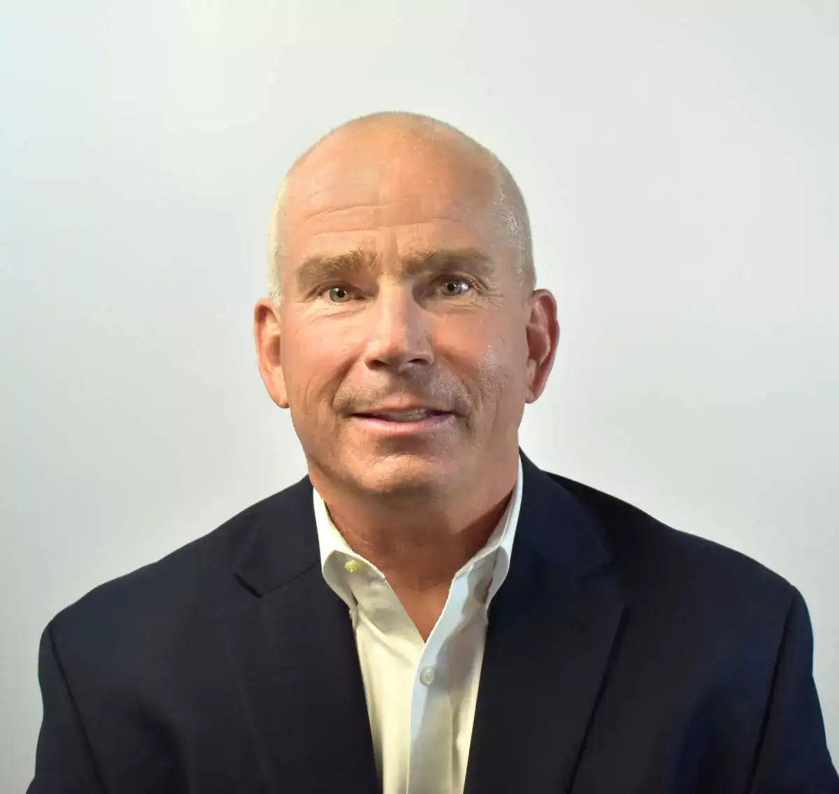 A professional portrait of a middle-aged man with a bald head, wearing a dark suit and white shirt, against a plain light background.