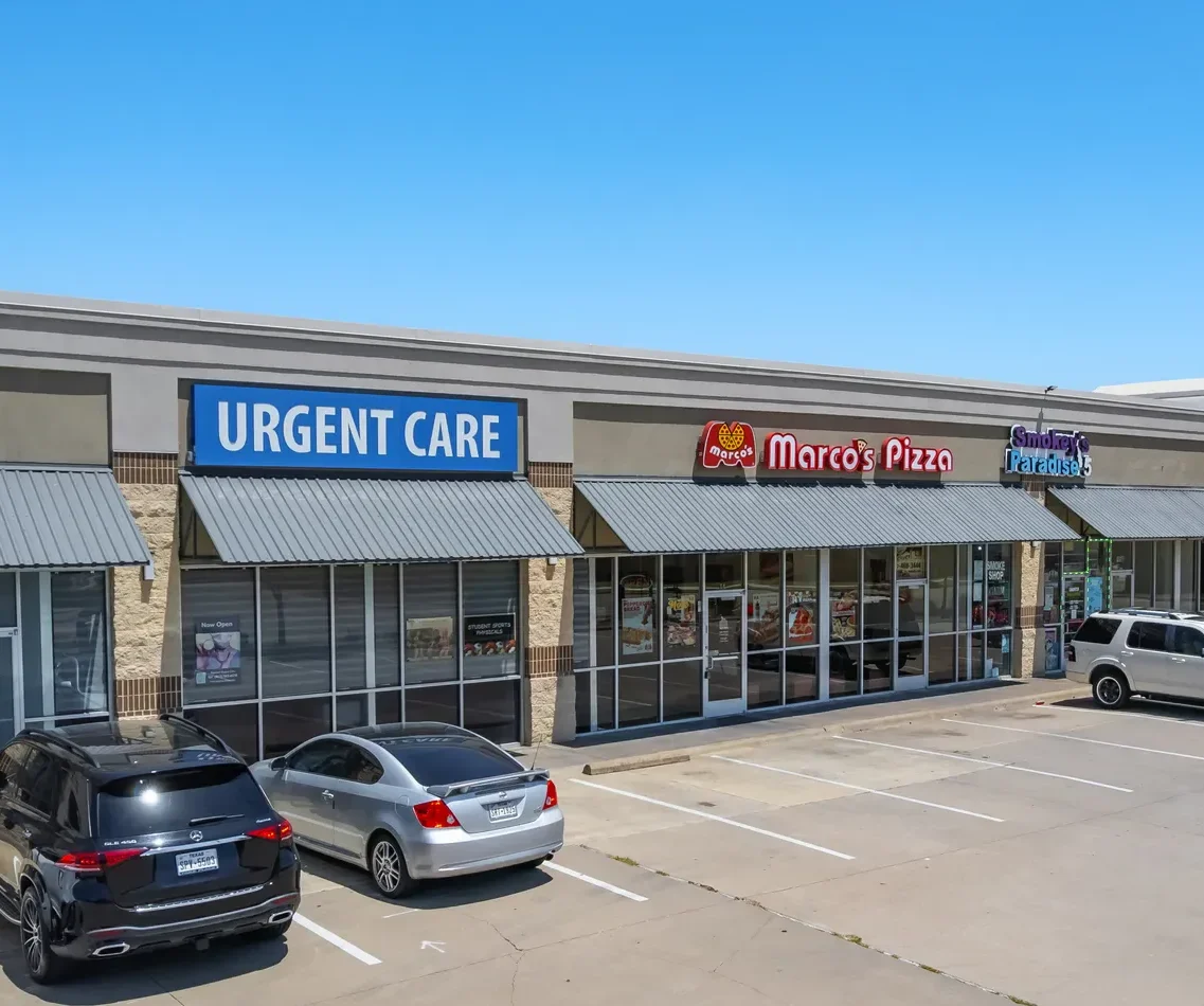 A shopping plaza featuring an urgent care center, Marco's Pizza, and other stores with parking spaces in front.