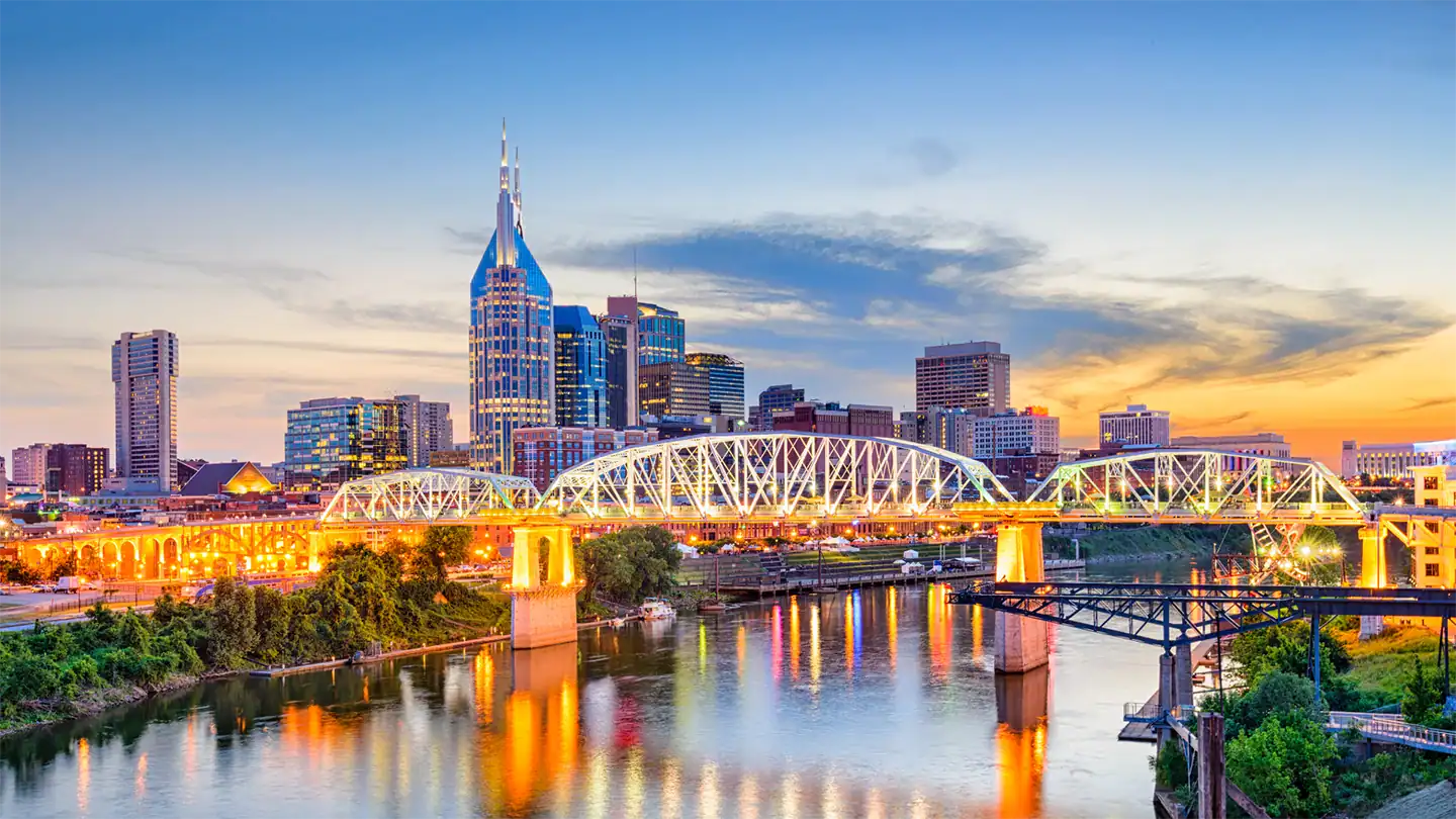 Nashville skyline at sunset featuring the AT&T Building and a lit-up bridge over the Cumberland River.