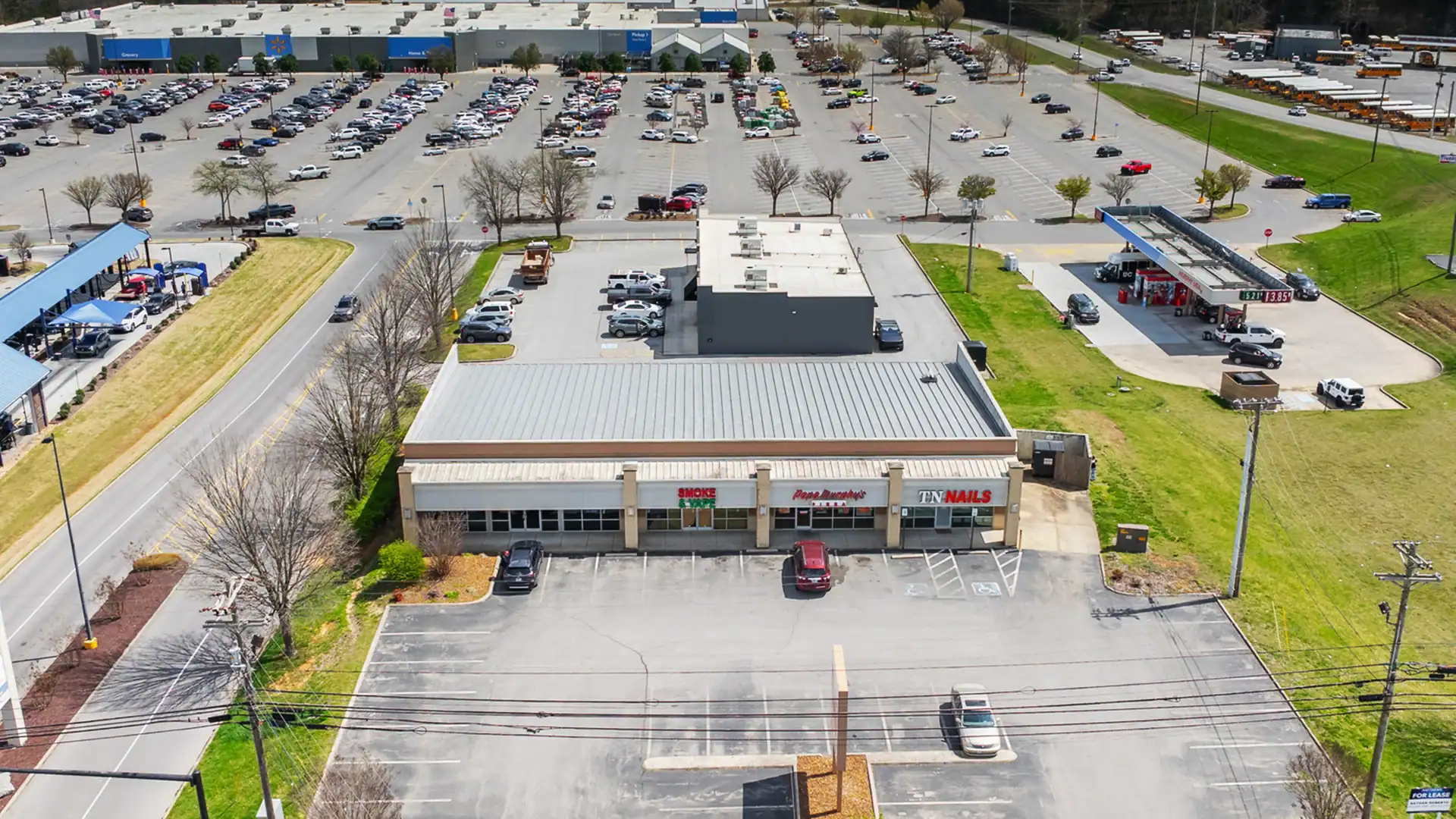 Aerial view of a shopping center parking lot with cars parked and surrounding green areas.
