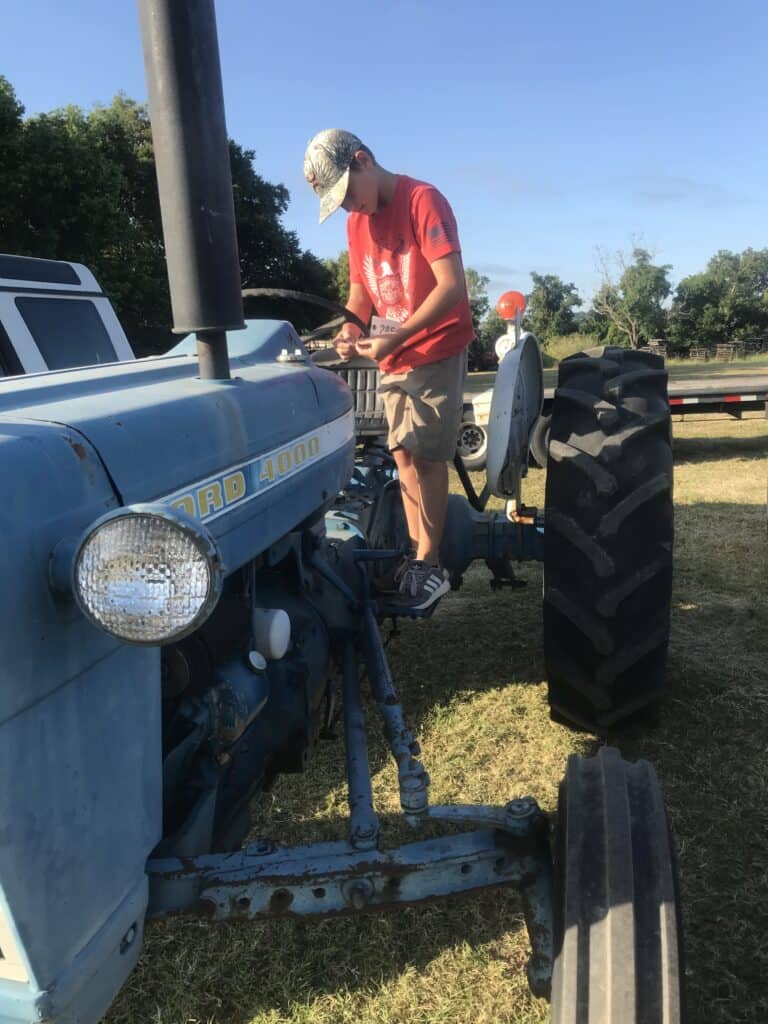 Classic blue tractor at Garrett Realty & Auction, featuring a young boy in a red shirt and cap stand.