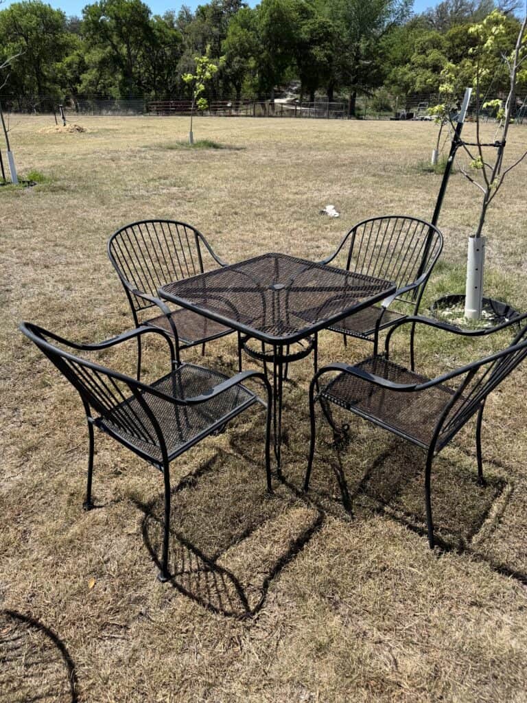 Outdoor metal patio table with four matching chairs in a grassy yard.
