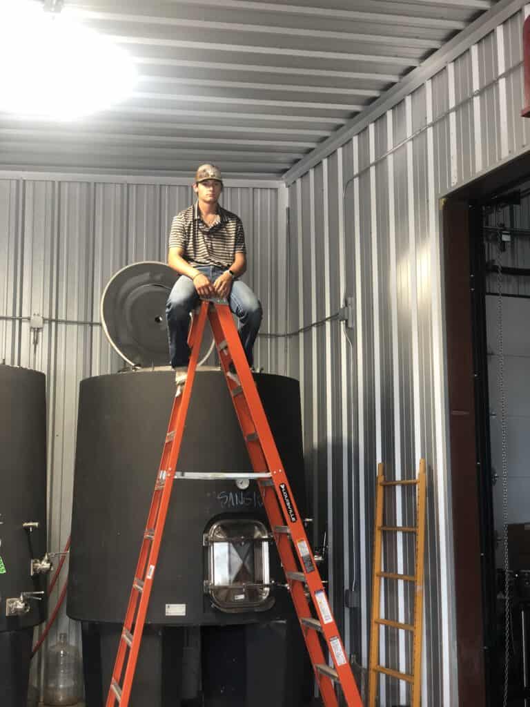 Man sitting on large industrial machine inside metal building.