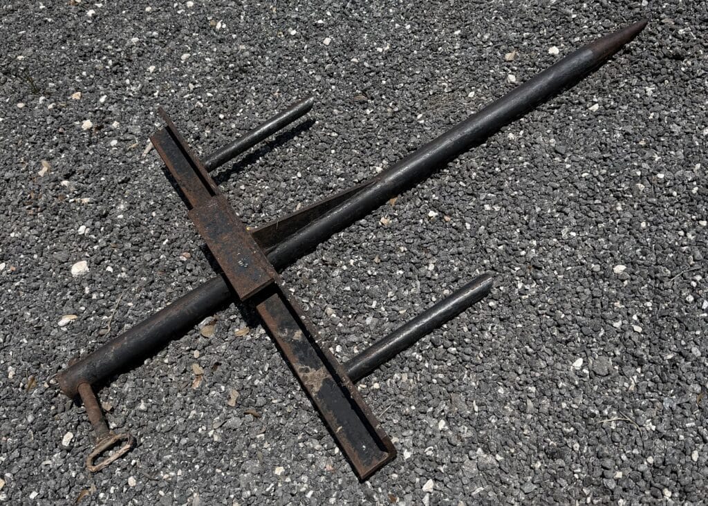 Rusty metal spear and stand on gravel surface.