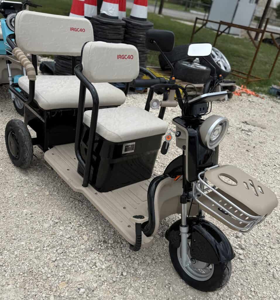 Electric mobility scooter with multiple seats and storage, outdoor setting.