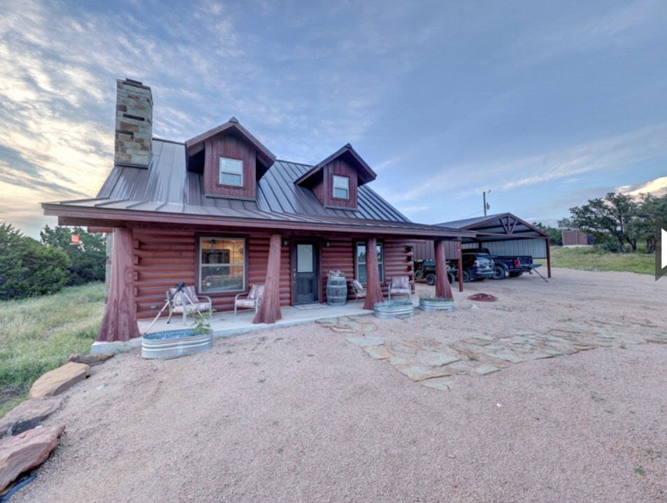 Rustic log cabin with metal roof and outdoor seating in a rural setting.