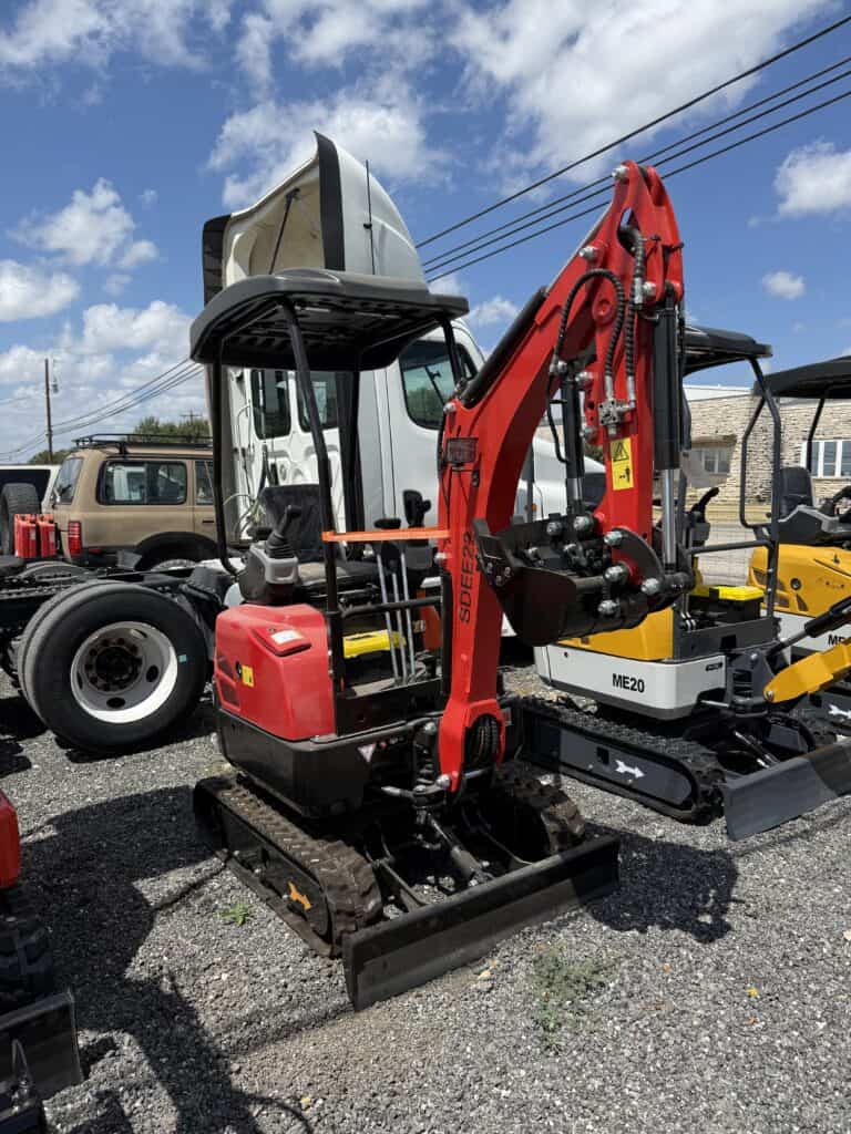 Red mini excavator at auction lot with other construction equipment.