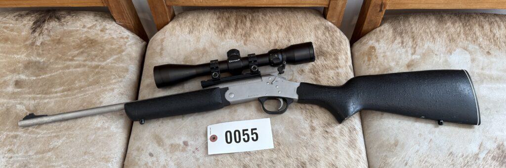 Black hunting rifle with scope on beige chair at auction.
