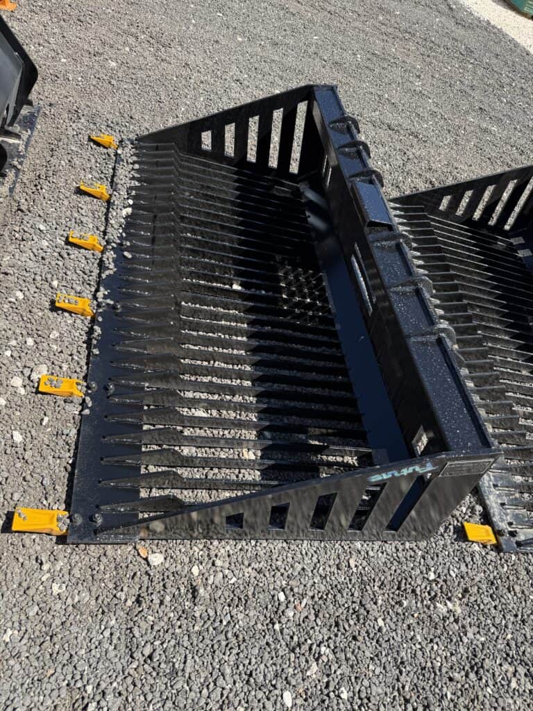 Black skid steer bucket attachment with yellow mounting brackets on gravel surface.