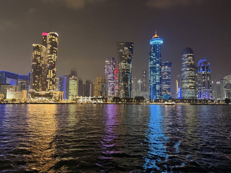 Vibrant cityscape featuring tall buildings and colorful lights along the waterfront.